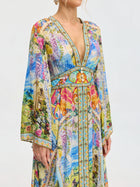 A woman wears the Social Queen Garden Print Silk Maxi Dress, a long-sleeved V-neck dress made from mulberry silk with vibrant garden-inspired and architectural patterns.
