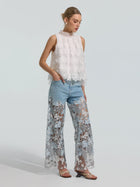 A woman stands against a plain light background wearing Social Queen’s Floral Lace Patchwork Pants paired with a sleeveless white lace top.