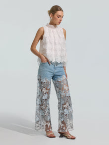 A woman stands against a plain light background wearing Social Queen’s Floral Lace Patchwork Pants paired with a sleeveless white lace top.