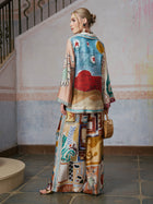 A woman stands indoors on a tiled floor near a staircase, holding a small woven bag and gazing to the side. She wears an artistic matching set that radiates effortless resort elegance, with the bold Abstract Print Mulberry Silk Shirt from Social Queen as the ensemble’s focal point.