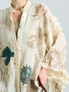 A person wearing the Social Queen Floral Embroidered Linen Jacket (Cami Included), featuring beige, green, and white floral embroidery, accessorized with a gold chain necklace.
