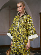 A woman stands indoors wearing the Social Queen Tropical Fruit Print Linen Dress, featuring a loose fit with wide sleeves and vibrant yellow and black patterns, reminiscent of a tropical robe, while holding a wooden handbag.