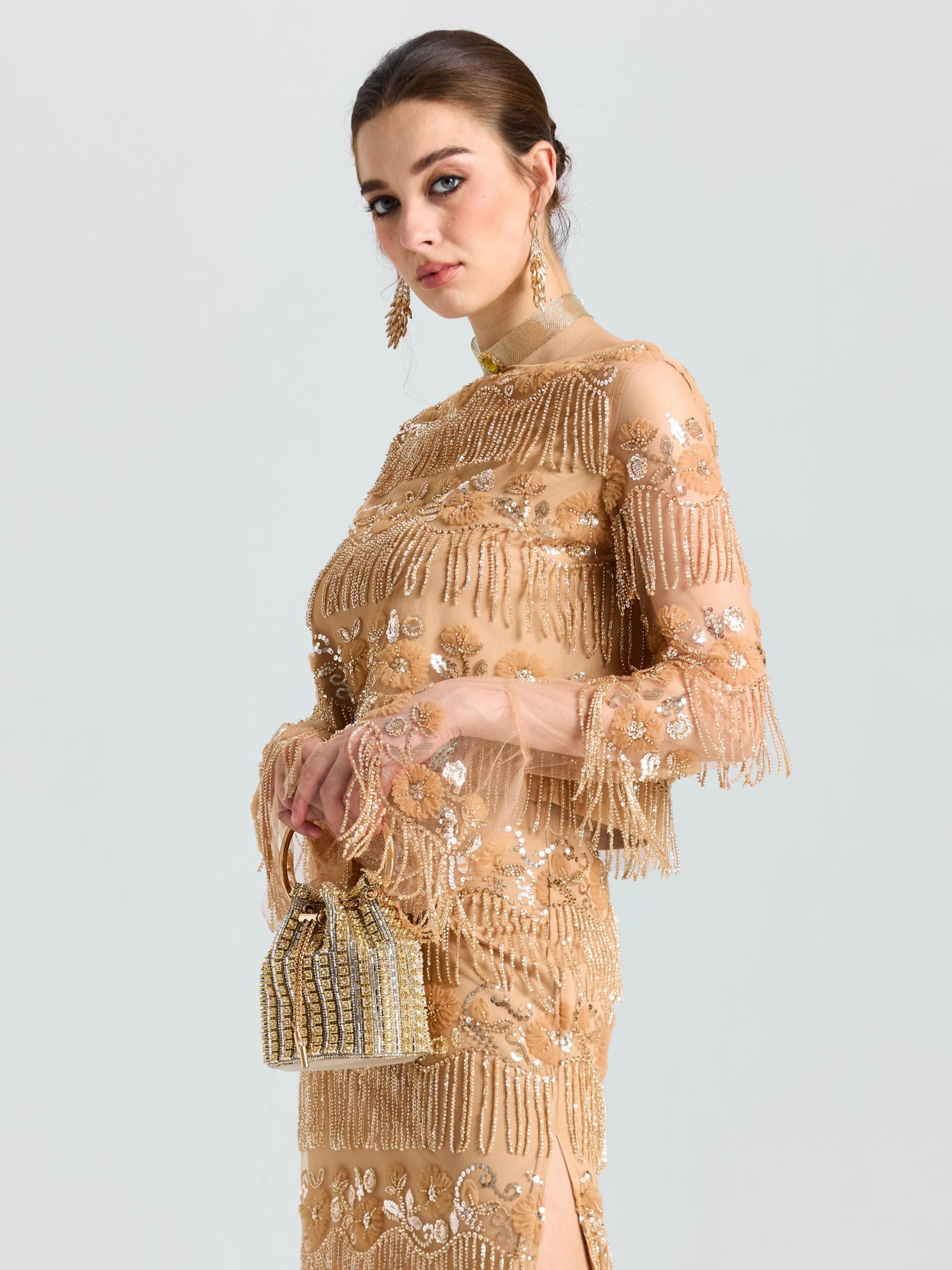 A woman wears the Social Queen Beaded Fringe Floral Top, paired with a gold embellished dress and small gold beaded handbag, posing against a plain light background.