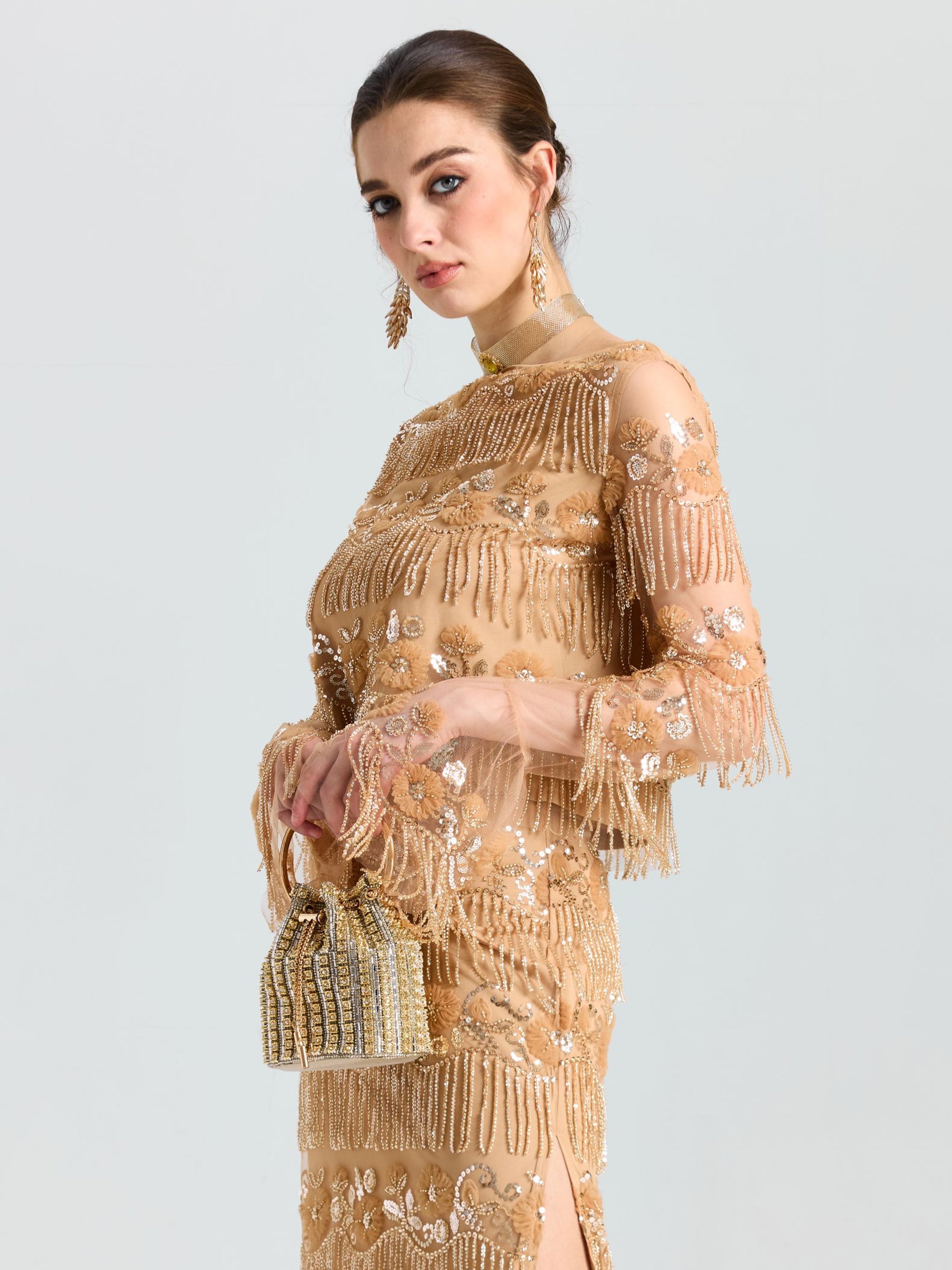A woman wears the Social Queen Beaded Fringe Floral Top, paired with a gold embellished dress and small gold beaded handbag, posing against a plain light background.