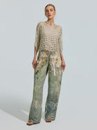 A woman wears the Social Queen Pearl Daisy Cutwork Top (camisole not included), featuring intricate pearl embellishments, paired with high-waisted, wide-leg jeans adorned with colorful beaded designs.