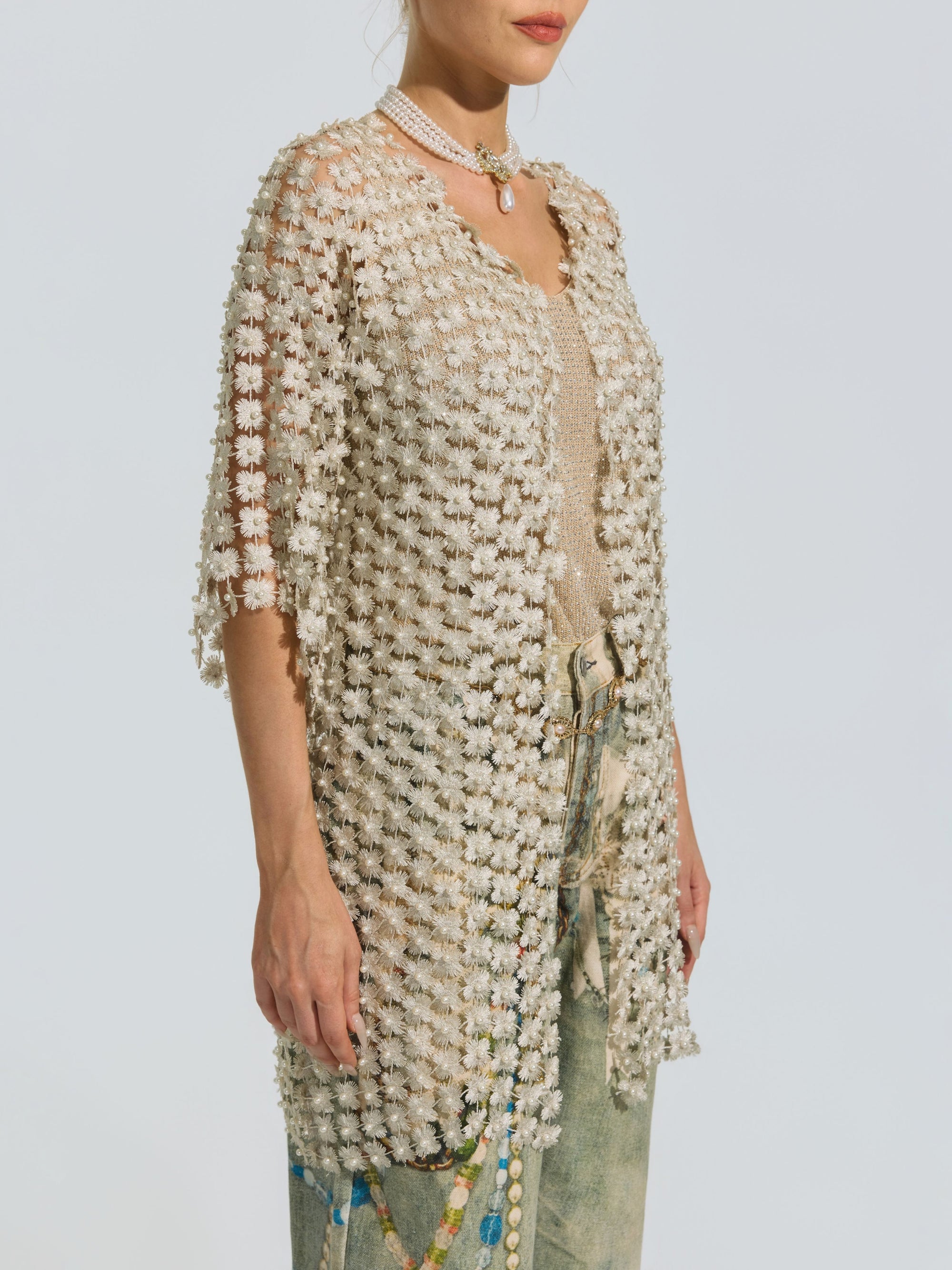 A woman styles the Social Queen Pearl Daisy Cutwork Long Cardigan (camisole not included)—a sheer, knee-length layer—with a beige top, faded jeans, and a pearl necklace.