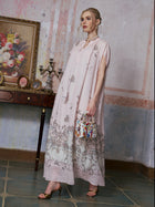 A woman wearing the Social Queen Baroque Garden Print Ramie Dress (includes slip dress) holds a colorful handbag as she stands indoors near a table decorated with ornaments and a framed floral painting.