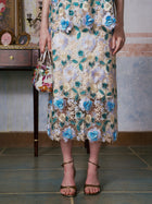 A person wearing the Social Queen 3D Floral Cutwork Lace Skirt, holding a small patterned handbag, stands indoors on a tiled floor.