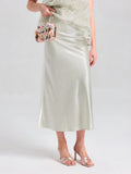 A person wearing the Social Queen Satin A-Line Midi Skirt in pale green with a matching top, open-toe heeled sandals, and holding a small floral-embellished handbag.