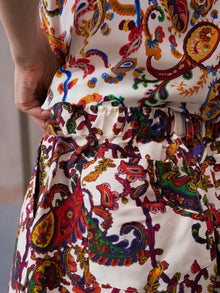 A person wearing Social Queen's Paisley Garden Print Silk Shorts featuring a gathered waistband—perfect for resort wear—with one hand resting on their hip.