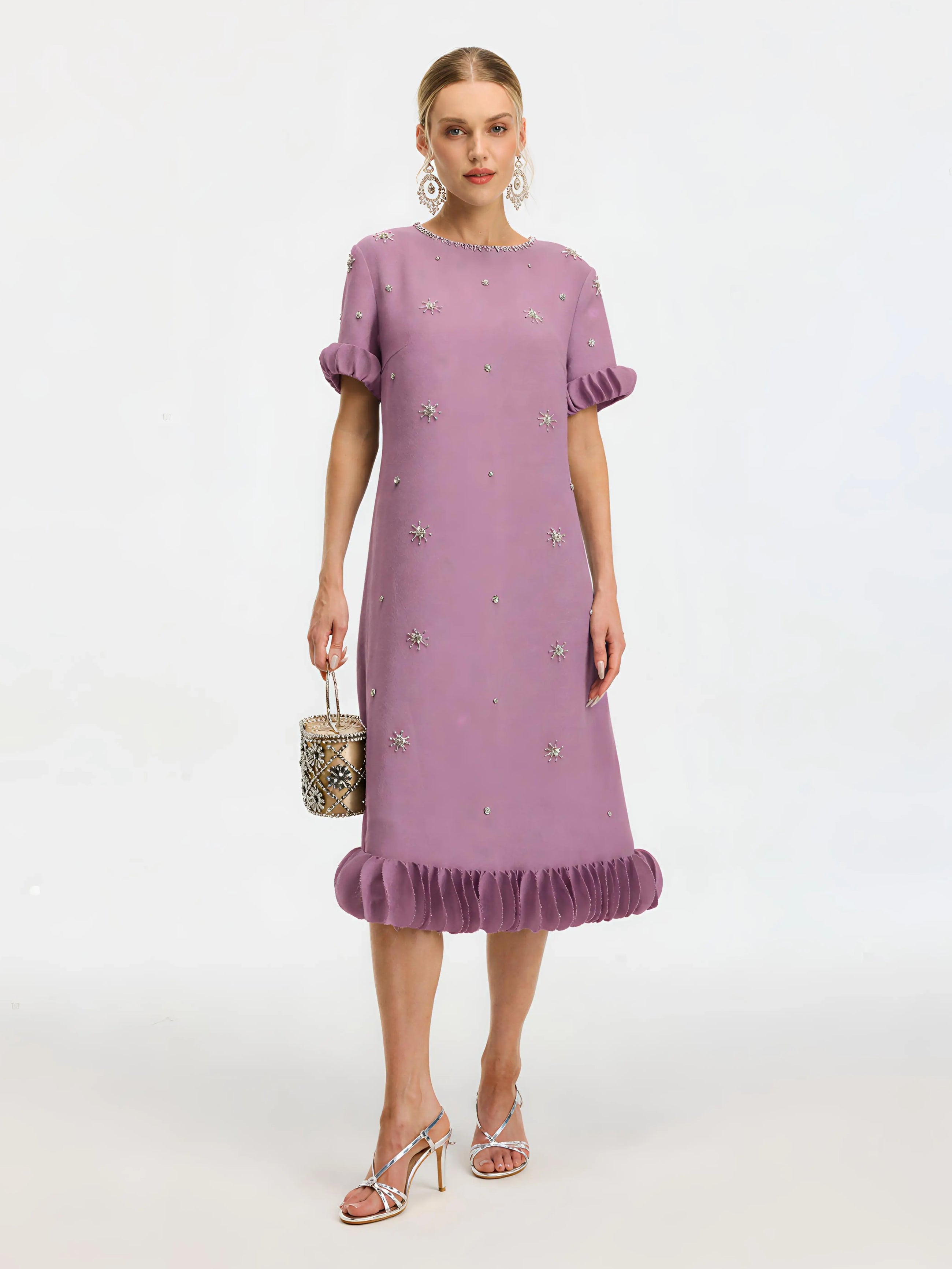 A woman wears the Social Queen Beaded Crystal Embellished Dress—a lavender, knee-length shift with a beaded neckline, ruffle hem and sleeves, and floral appliqués—paired with a round bag, strappy heels, and statement earrings.