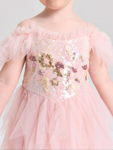 A young child wears the Social Queen Girls Floral Sequin Tulle Dress, featuring light pink tulle sleeves and gold, pink, and silver embellishments on the floral sequin bodice.