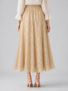 A person stands facing away, wearing a cream blouse with ruffled sleeves and the Social Queen Jacquard Chiffon Midi Skirt, featuring a beige jacquard texture and elastic waist, elegantly paired with light strappy heels.