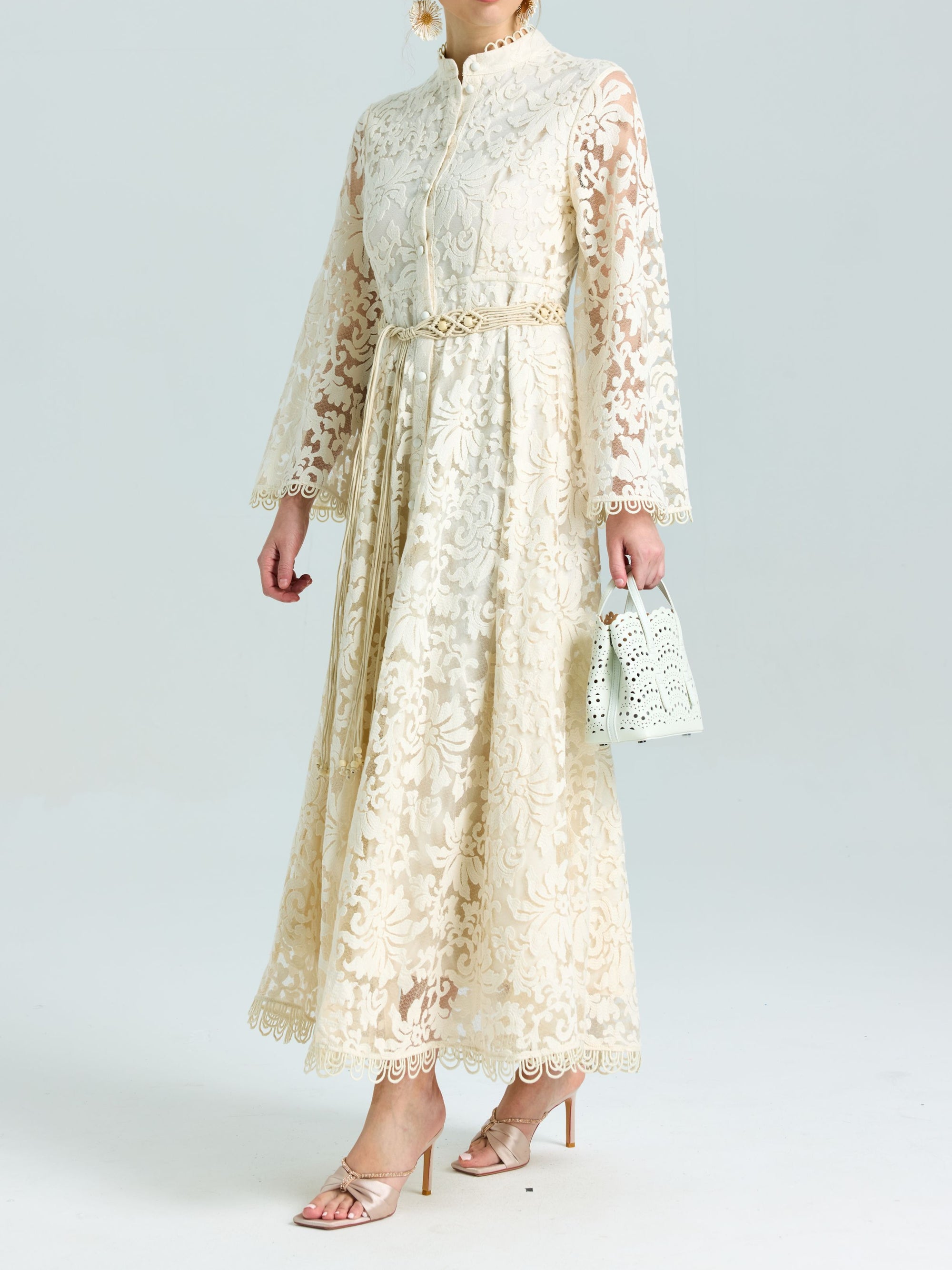 A woman wears the Social Queen Embroidered Lace High-Neck Dress—cream, baroque floral, belted waist, lace-effect embroidery—with a white handbag and open-toe heels, making it the perfect special occasion look.