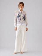A woman stands against a plain background wearing Social Queen’s Casual Wide-Leg Pants in white, paired with white sandals and a sheer floral embroidered blouse.
