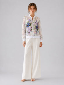 A woman stands against a plain background wearing Social Queen’s Casual Wide-Leg Pants in white, paired with white sandals and a sheer floral embroidered blouse.
