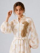 A woman wearing the Social Queen Leaf Embroidered Beaded Dress, featuring gold embroidery, a belt, and gold beaded embellishment on the chest, stands against a plain light background.