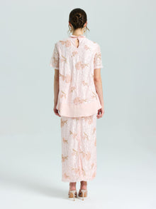 A woman stands facing away, wearing the Social Queen Dragonfly Beaded Lace Top in light pink with delicate embroidery and a matching long skirt. Her hair is up and she completes the look with nude heels.