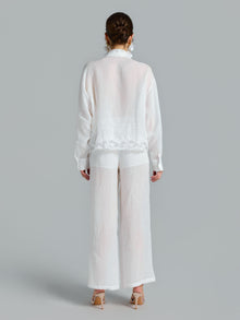A person is shown from the back against a gray background, wearing the Social Queen 3D Lace Appliqué Shirt in a sheer white, relaxed long-sleeve style paired with wide-leg pants.