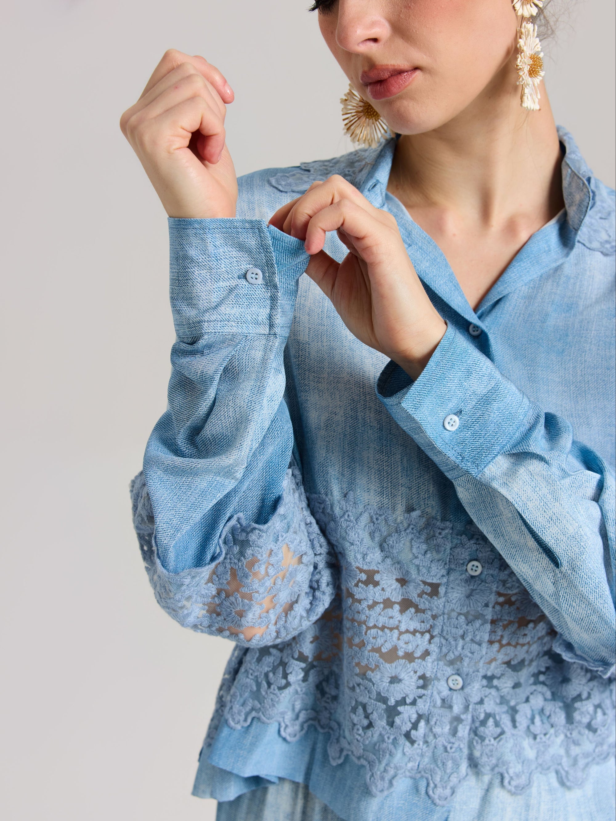 A woman in the Social Queen Washed Silk Lace Detail Shirt, a relaxed fit light blue blouse with lace trim, fastens a cuff button. Only her upper body is visible against a plain background.