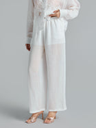 A person wearing Social Queen Textured Straight-Leg Pants in sheer white with a relaxed silhouette, a white lace top, and nude high-heeled sandals stands against a plain gray background.