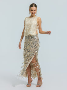 A woman stands against a plain light background wearing the Social Queen Floral Beaded Mesh Sleeveless Top, a sleeveless cream mesh design embellished with delicate beading, paired with a silver sequin fringe skirt and high-heeled sandals.