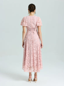 A woman faces away, wearing the Social Queen Floral Embroidered Lace Dress in light pink with short sleeves and lace-up back detail, paired with nude heeled sandals.