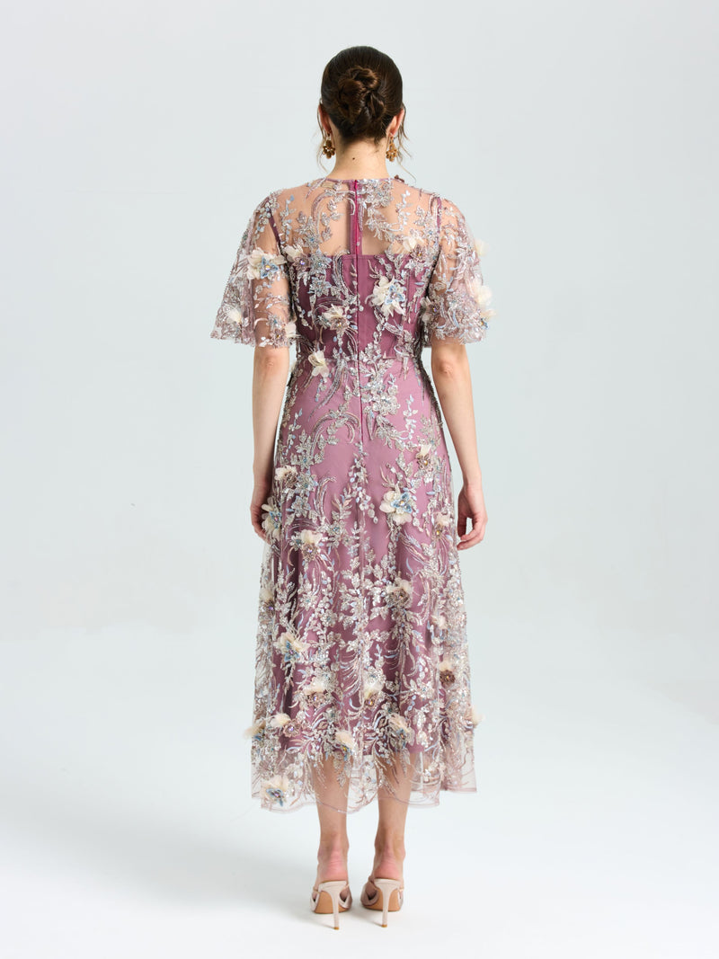 A woman faces away, wearing the Social Queen Floral Beaded A-Line Dress with sheer flutter sleeves. Her brown hair is in a low updo, and she pairs the look with heels.