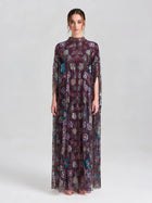 A woman poses in a studio wearing the Social Queen Beaded Floral Embellished Cape Gown—an elegant long, sheer purple gown with floral sequins and short sleeves—set against a neutral background.