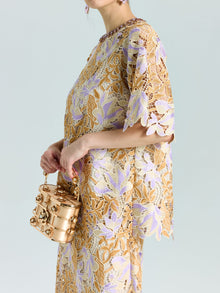 A person wears the Social Queen Floral Embroidered Lace Top, styled with a gold metallic handbag featuring a beaded handle, against a plain background.