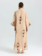 A person stands facing away, wearing the Social Queen Placement Embroidered Linen Dress with wide sleeves and brown damask scroll embroidery, paired with high-heeled sandals.