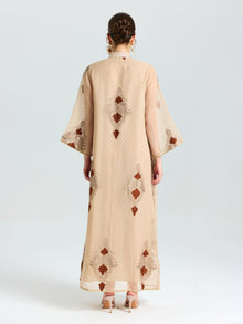 A person stands facing away, wearing the Social Queen Placement Embroidered Linen Dress with wide sleeves and brown damask scroll embroidery, paired with high-heeled sandals.