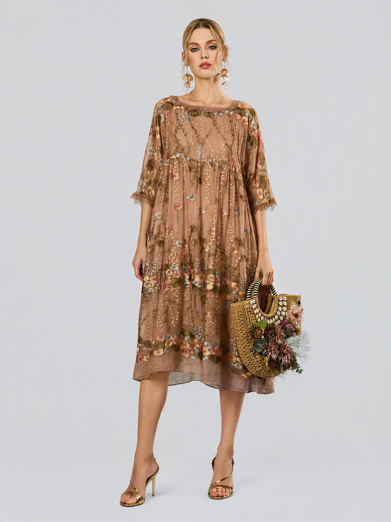 A woman models the Social Queen Square-Neck Embroidered Silk Dress—featuring airy sheer fabric, floral embroidery, three-quarter sleeves, and a delicate square neckline—styled with heeled sandals and a decorative straw handbag against a plain backdrop.