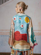 A person with blonde hair in a low bun wears the Social Queen Abstract Print Mulberry Silk Shirt, standing with their back to the camera against a light, textured wall.