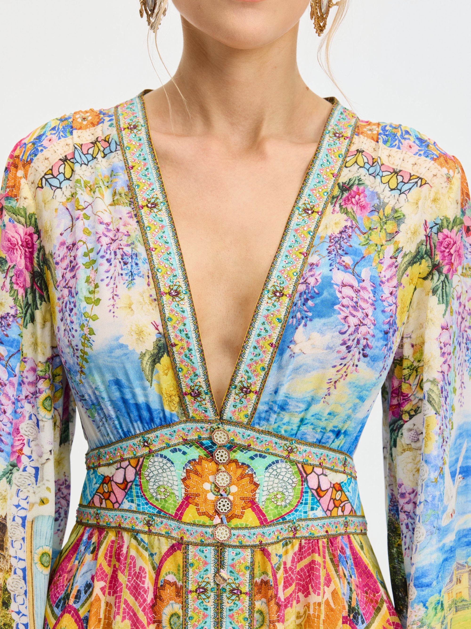 A woman wears the Social Queen Garden Print Silk Maxi Dress, featuring a vibrant garden pattern, deep V-neckline, and decorative trim.
