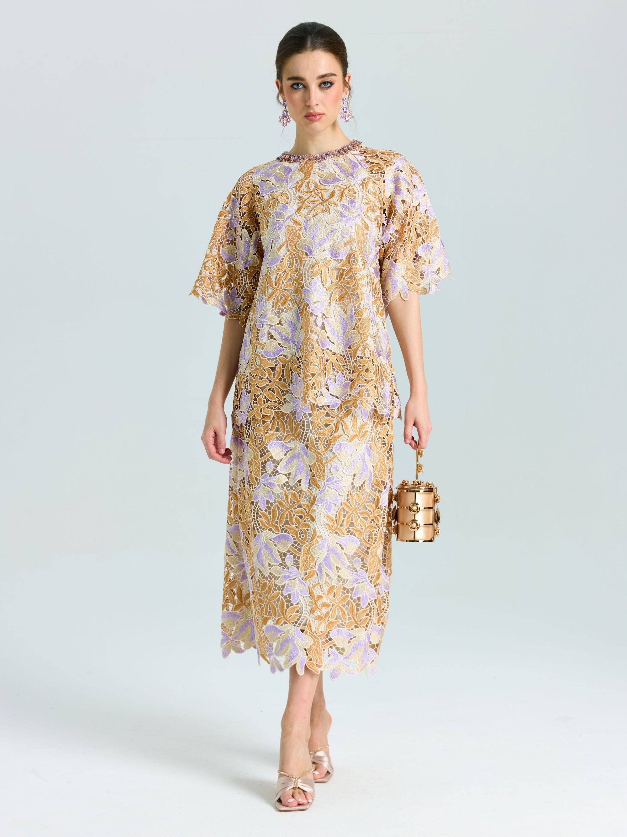 A woman styles the Social Queen Floral Embroidered Lace Midi Skirt in gold and lavender with a small cylindrical handbag and heeled sandals—an elegant look perfect for evening occasions.