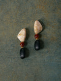 Social Queen Multicolor Beaded Drop Earrings, featuring irregular cream stones, round brown beads, and matte black oval drops, are displayed on a textured green surface.