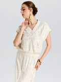 Woman in a Social Queen Floral Embroidered Linen Top with short sleeves, paired with a skirt, tassel earrings, and a bangle, standing against a plain background.