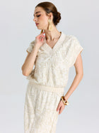 Woman in a Social Queen Floral Embroidered Linen Top with short sleeves, paired with a skirt, tassel earrings, and a bangle, standing against a plain background.