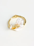 The Social Queen Magnolia Petal Cuff Bracelet features an abstract, pearl-like white accent on gold, inspired by natural petals and displayed on a plain white background.