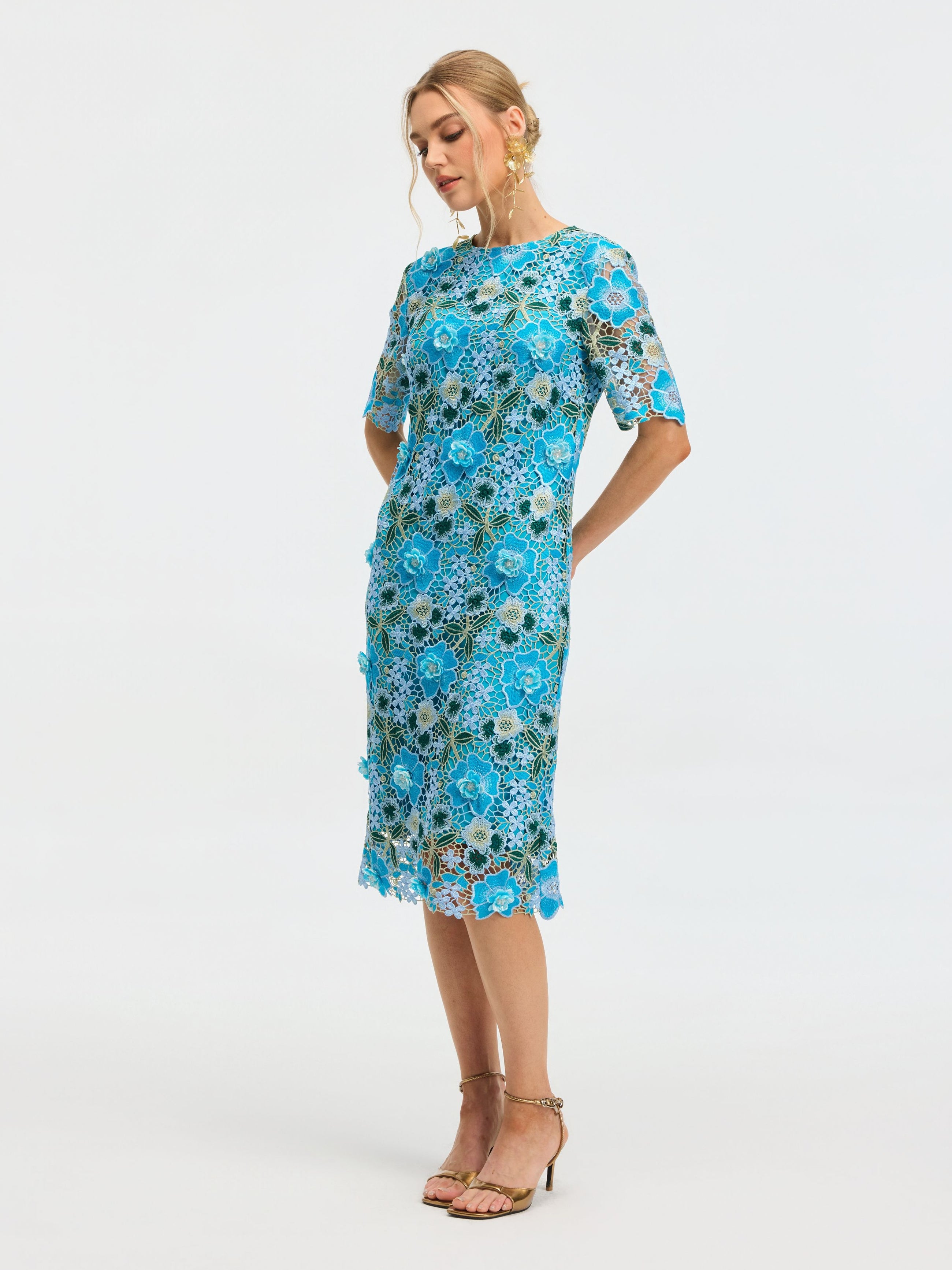 A woman stands in profile against a plain white background wearing the Social Queen Floral Appliqué Lace Shift Dress with short sleeves and tan high-heeled sandals.