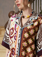 A woman wears the Social Queen Patchwork Print Cotton Shirt Dress, which features geometric, swirl, and zebra designs; she accessorizes with a multicolored beaded necklace and a statement earring. Stairs and a railing appear in the background.