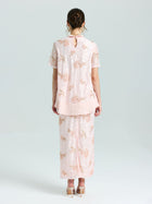 A woman stands with her back to the camera wearing Social Queen’s Dragonfly Beaded Lace Midi Skirt and matching top in light pink, both embellished with delicate beadwork, set against a simple pale background.