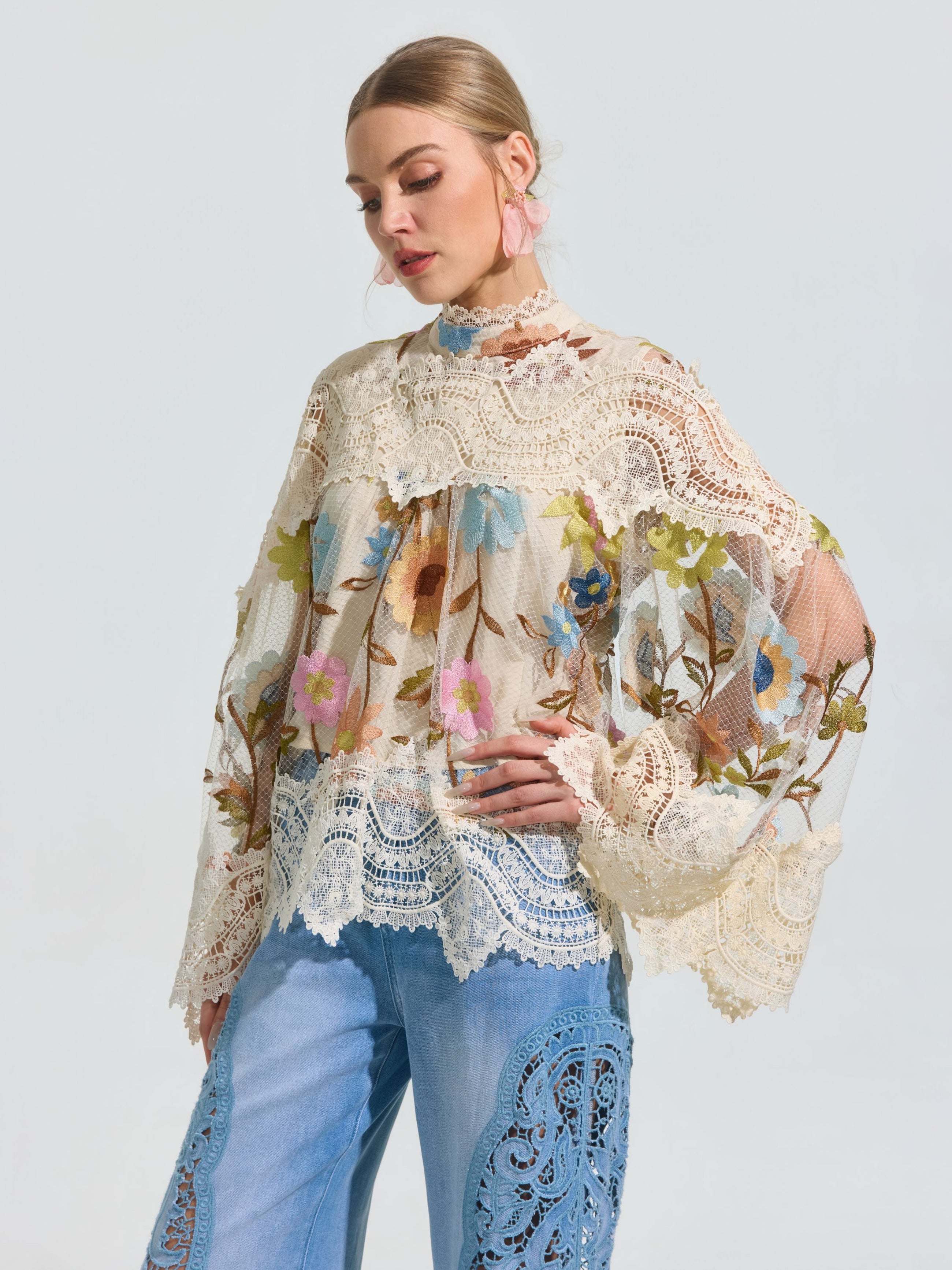 A woman wears the Social Queen Floral Embroidered Lace Trim Top with wide sleeves and pairs it with blue lace-detailed jeans, standing against a plain light background.