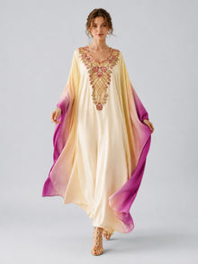 A woman wears the Social Queen Ombré Beaded Embroidered Cape Dress—a long satin gown with cream-to-purple ombré coloring and intricate chest embroidery—paired with gold sandals, standing against a plain light gray background.