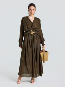 A woman models the Social Queen Twist-Front Ramie Shirt, featuring long sleeves and a twist-front waist, paired with a tan handbag and open-toe heels against a plain light background.