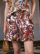 Dressed in Social Queen’s Paisley Garden Print Silk Shorts and matching shirt, this look—paired with a small woven bag and shown on a checkered floor—captures effortless resort wear style.
