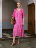 A woman stands indoors near a wooden door, wearing the Social Queen Geometric Jacquard Mulberry Silk Dress with tan sandals and carrying a colorful woven bag on a tiled floor—an ideal look for effortless resort wear.