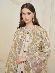 A woman with long brown hair wears the Social Queen Italian Baroque Floral Metallic Jacquard Jacket with large buttons and ornate earrings, standing against a textured cream-colored wall.