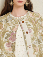 A woman wears the Social Queen Italian Baroque Floral Metallic Jacquard Jacket with brown buttons over a pearl-embellished white top, paired with ornate gold earrings.